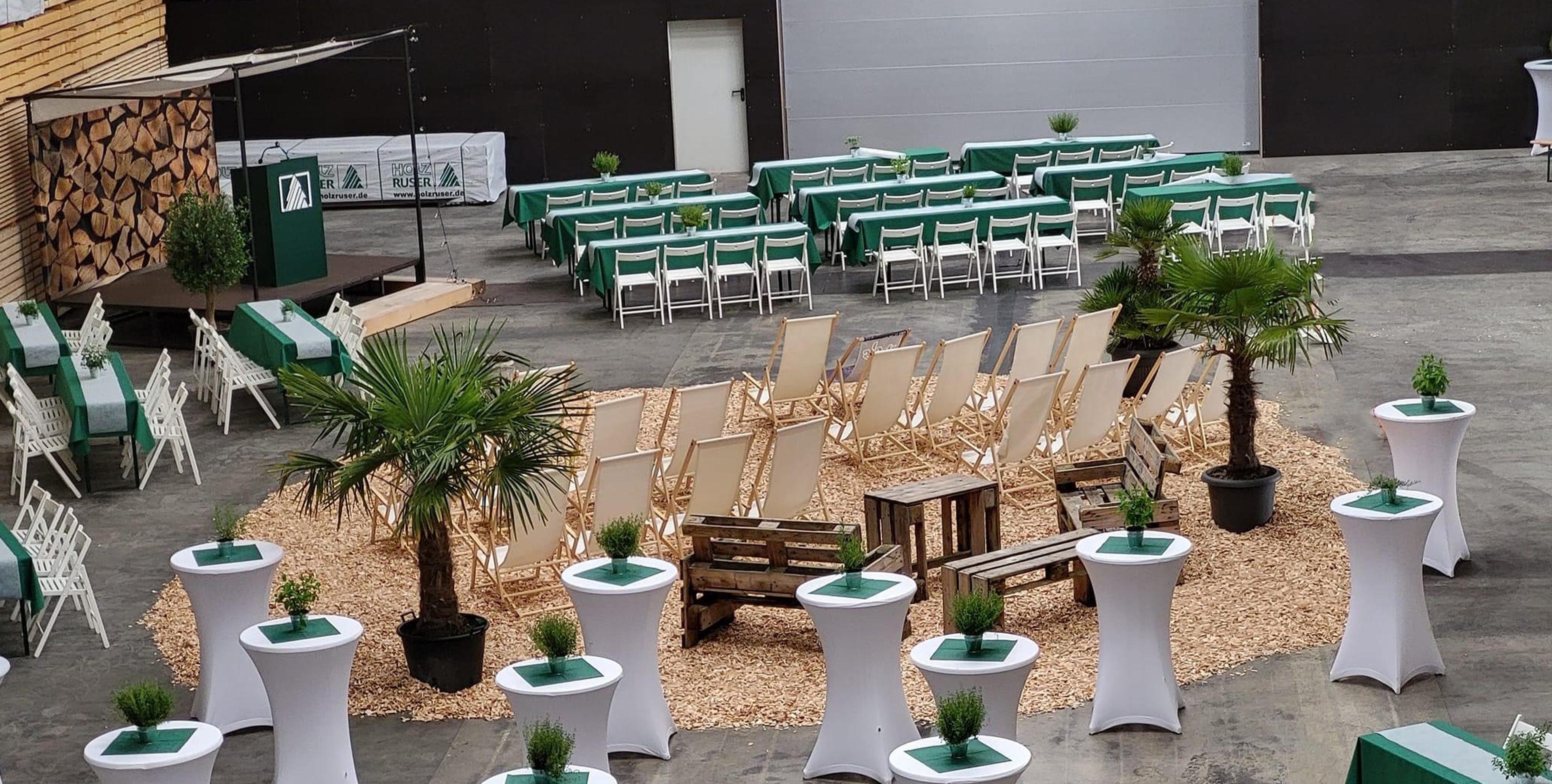 Firmenfeier mit Lounge-Möbeln, Bierzeltgarnituren, kleiner Bühne und passender Dekoration – hochwertige Eventausstattung für Firmenevents.