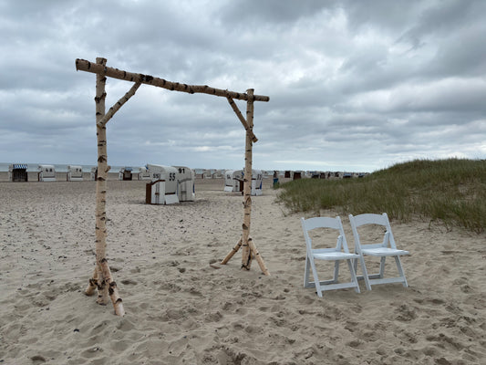 Traubogen aus Birkenstämmen bei einer freien Trauung am Strand – natürlich dekoriert mit Tüll und Blumen vor maritimer Kulisse
