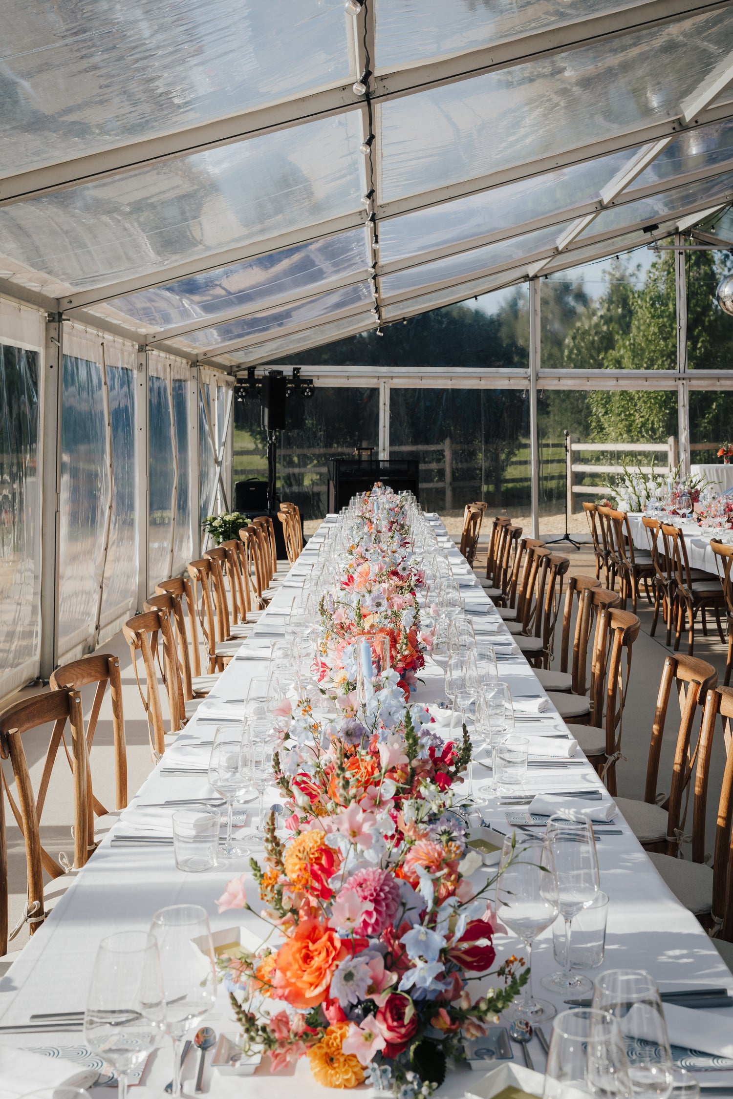 Eingedeckte Hochzeitstafel im Festzelt mit weißer Tischwäsche, floraler Dekoration und vollständig vorbereitetem Eventsetup